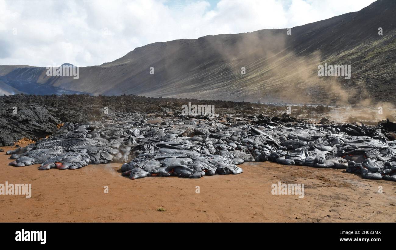 La coulée de lave de Pahoehoe dans la vallée de Nátthagi en Islande.La croûte de lave est grise et noire, la lave fondue est rouge.La montagne en arrière-plan, et la vapeur poussiéreuse s'élève. Banque D'Images