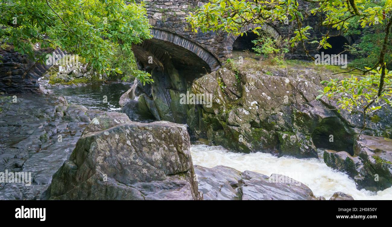 De l'eau mousseuse blanche coule au-dessus de la cascade et se dirige vers le pont en y-pair sur l'Afon Llugwy, Betws-y-coed, parc national de Snowdonia, pays de Galles Banque D'Images