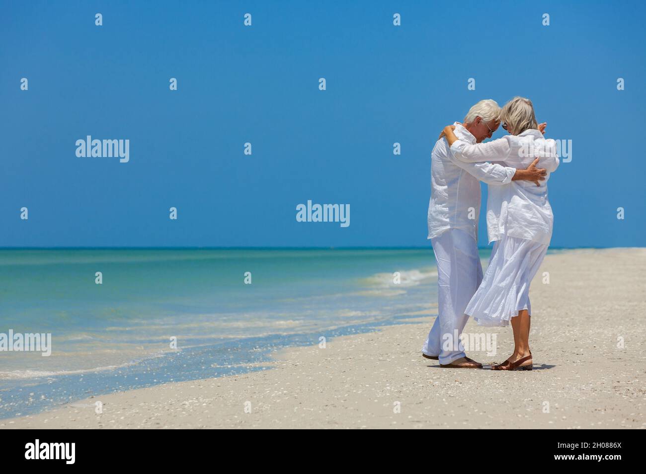 Un homme et une femme heureux ont pris leur retraite en vacances dansant sur une plage tropicale déserte avec un ciel bleu clair et lumineux Banque D'Images