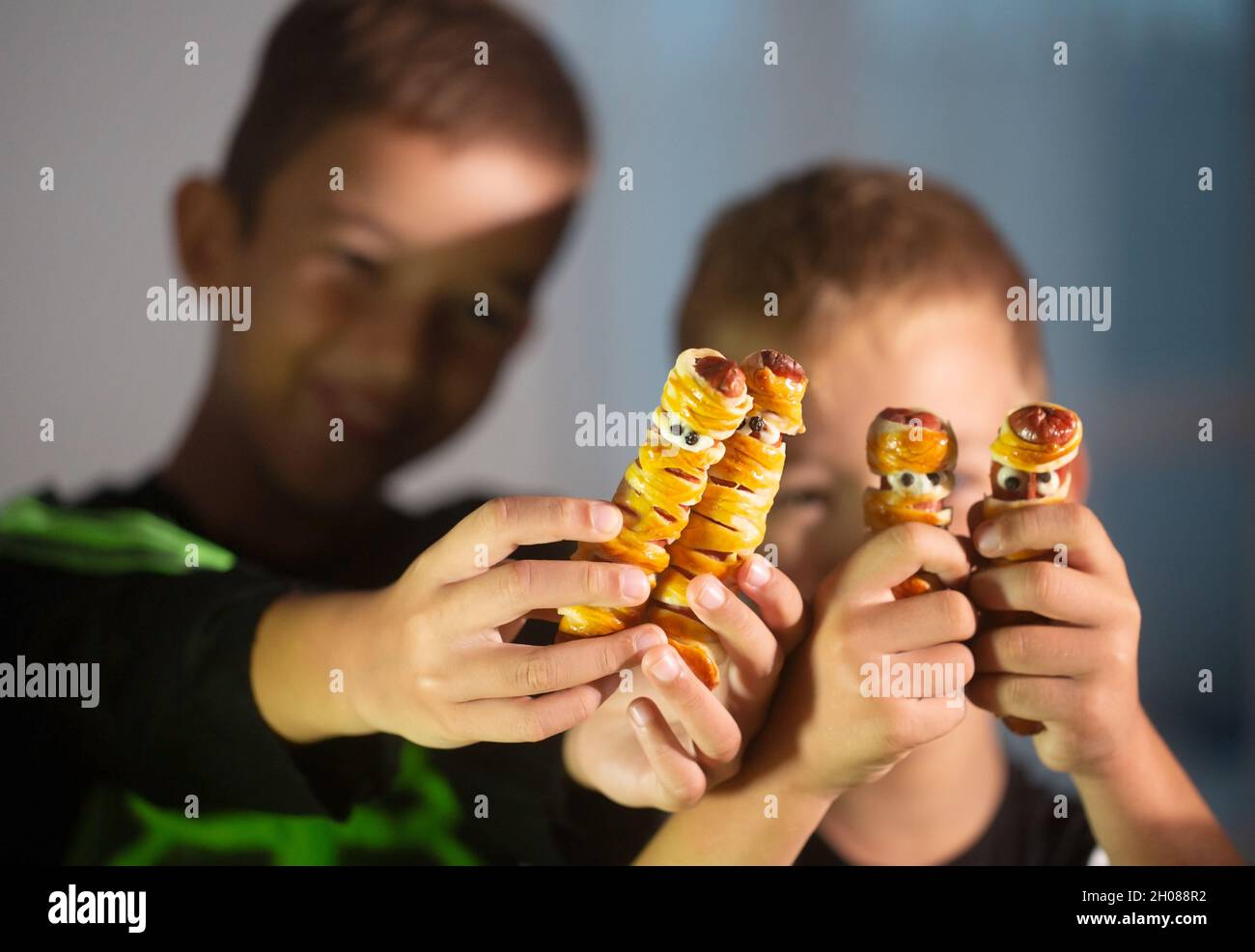 Deux enfants heureux tenant des collations de Halloween en forme de momie faites de saucisse Banque D'Images