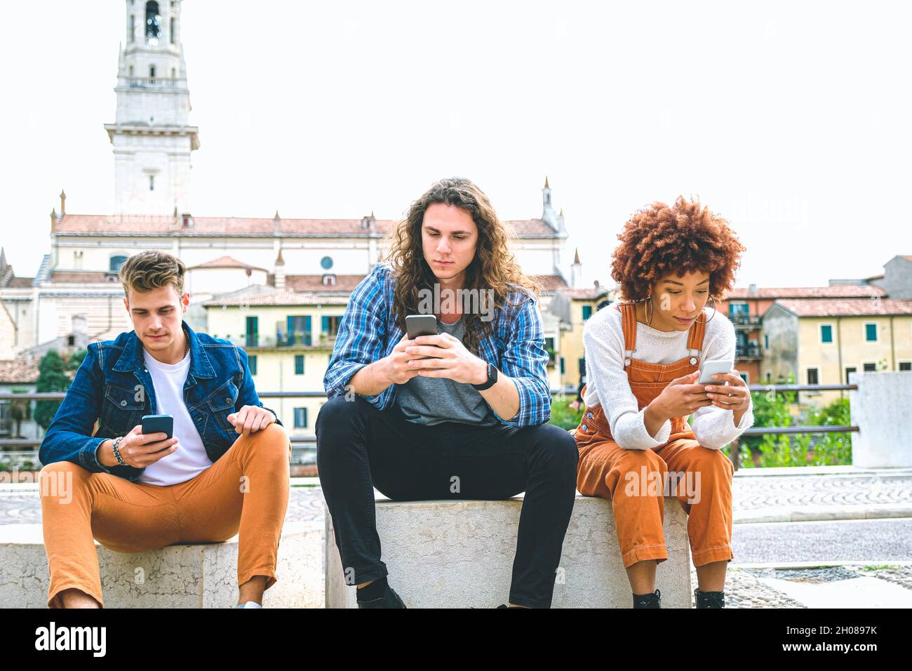 Groupe multiculturel d'amis utilisant des téléphones mobiles - étudiants assis dans une rangée et tapant sur un smartphone Banque D'Images