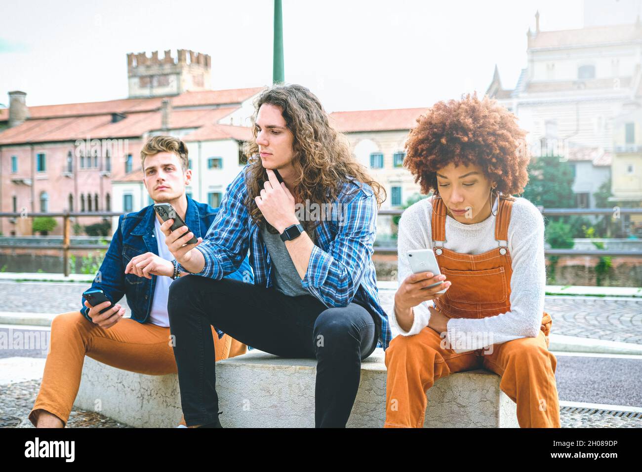 Groupe multiculturel d'amis utilisant des téléphones mobiles - étudiants assis dans une rangée et tapant sur un smartphone Banque D'Images