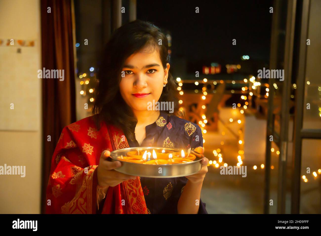 Portrait de Happy Young indian magnifique femme tenir plaque/thali avec diya/argile lampes à l'huile portant la robe traditionnelle, célébrant diwali, à la maison.Pretty fe Banque D'Images