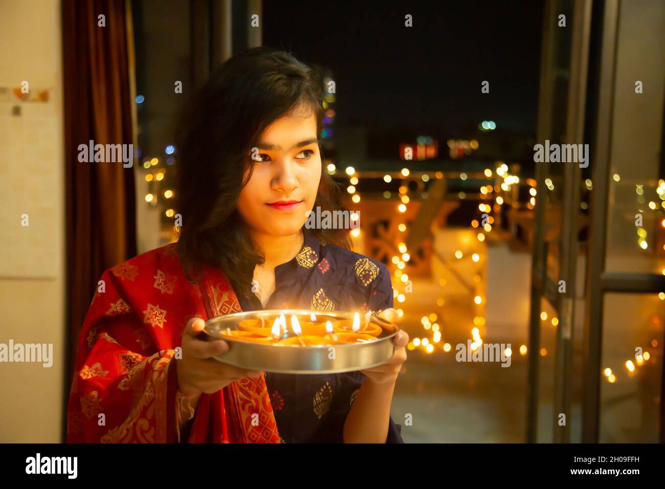 Happy Young indian magnifique femme tenir plaque/thali avec diya/argile lampes à l'huile portant la robe traditionnelle, célébrant diwali, festival de lumières, à la maison.Pr Banque D'Images