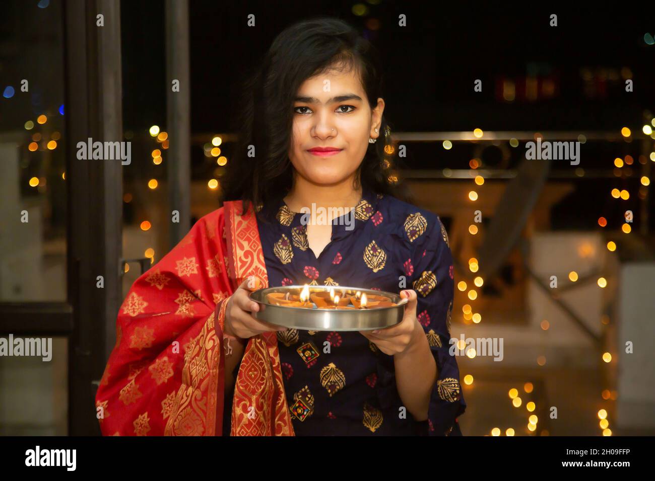 Portrait de Happy Young indian belle femme tenir plaque/thali avec diya/argile lampes à l'huile portant la robe traditionnelle, célébrant diwali, intérieur.Pretty fe Banque D'Images