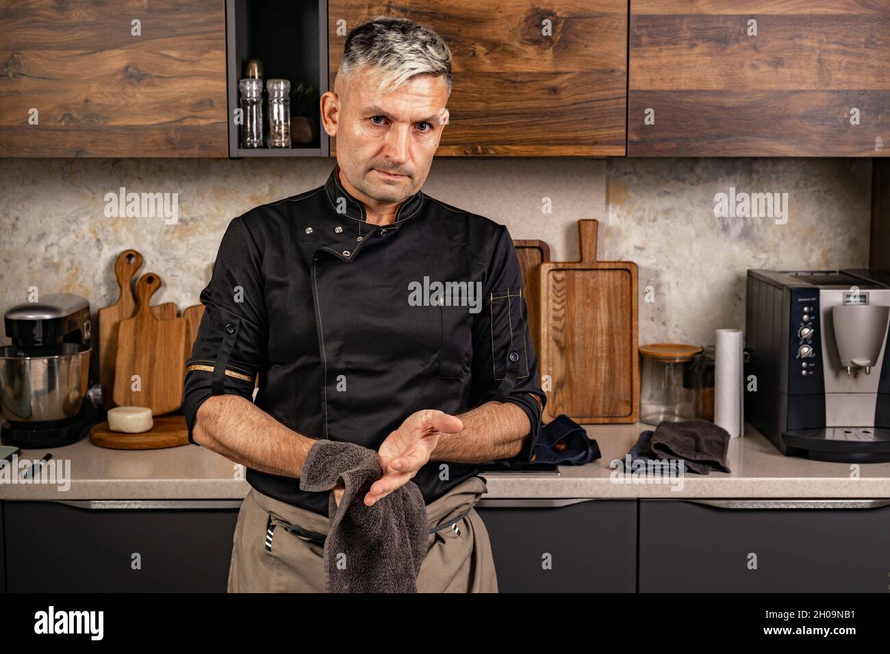 Portrait un charmant chef élégant dans une veste noire essuie ses mains avec une serviette.Le chef gai de l'ethnie caucasienne prépare de la nourriture dans sa cuisine.PE Banque D'Images