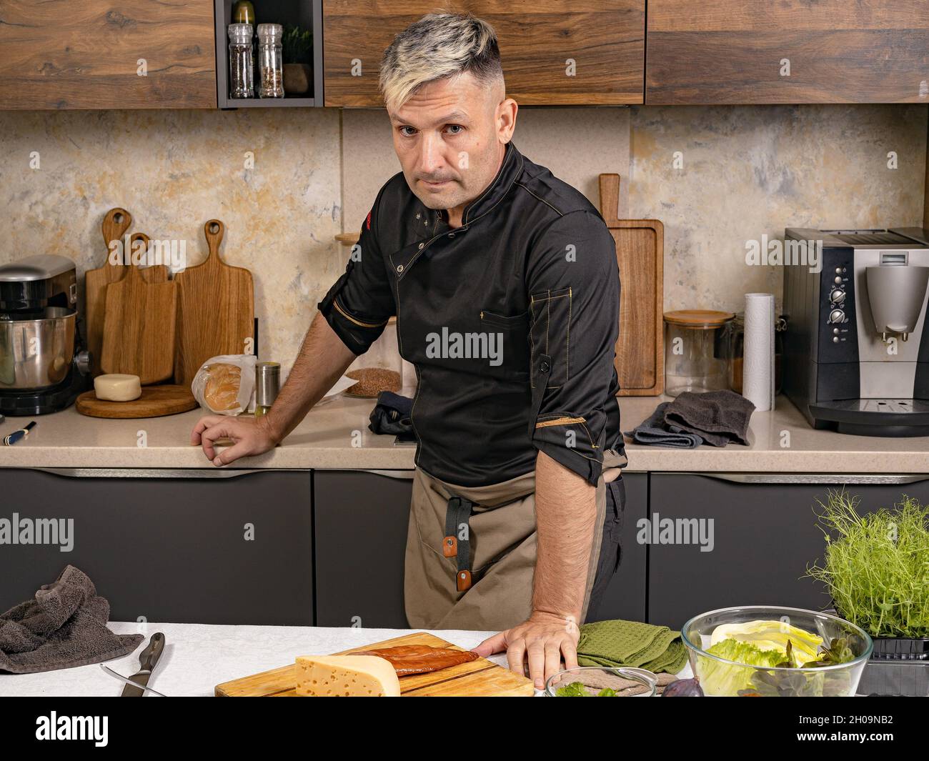 Portrait un chef élégant dans une veste noire pose dans sa cuisine.Le chef gai de l'ethnie caucasienne prépare de la nourriture dans sa cuisine.Les gens au travail.Prof Banque D'Images