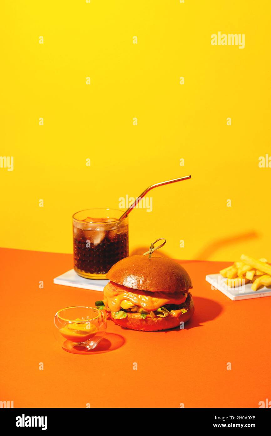 Grand hamburger avec frites et sauce sur fond orange et jaune vif. Restauration rapide américaine. Banque D'Images