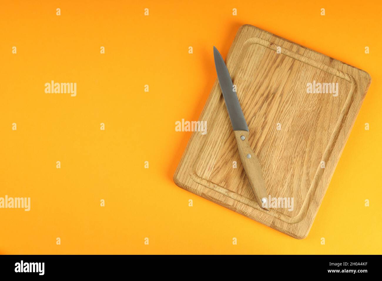 Planche à découper avec couteau sur fond orange. Banque D'Images
