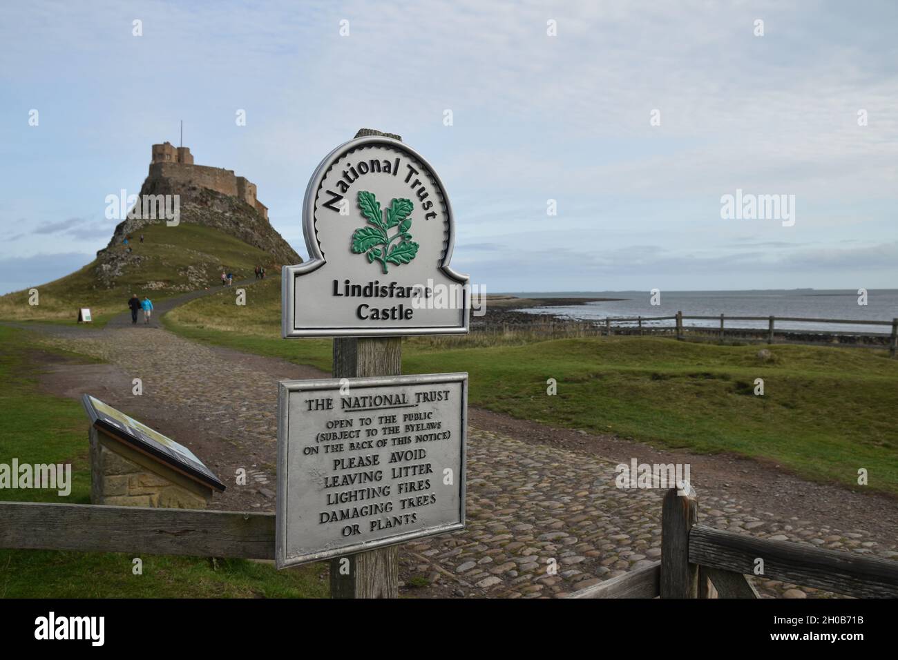 Panneau pour le château de Lindisfarne avec fond flou de chemin, château et ciel bleu avec des nuages.Faible profondeur de champ. Banque D'Images