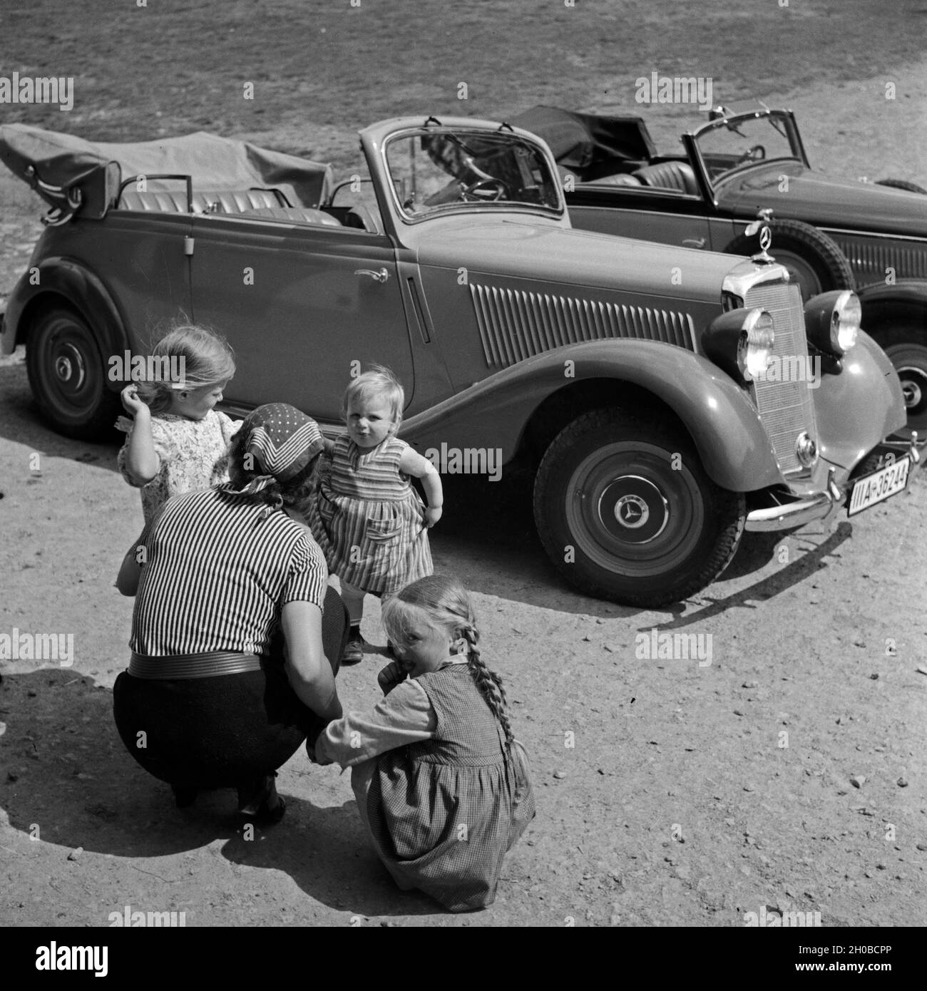 Eine Frau mit drei kleinen Mädchen auf einem Parkplatz vor einem Mercedes Benz 170 V (136 W) en Freudenstadt im Schwarzwald, Deutschland 1930 er JAhre. Une femme avec trois filles bambin devant une Mercedes Benz 170 V (136 W) à Freudenstadt en Forêt Noire, Allemagne 1930. Banque D'Images