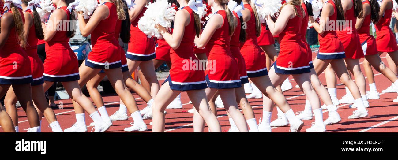 Les meneurs de l'école secondaire portant des uniformes rouges et blancs applaudissent tout en tenant des pompons pendant un match de football en salle. Banque D'Images