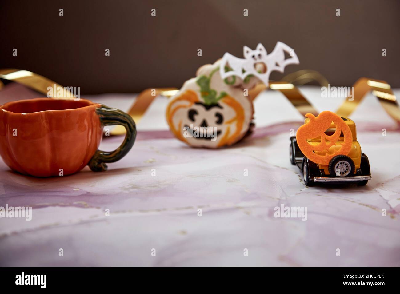 Décors d'Halloween avec mug à motif citrouille orange, biscuit à la main, citrouilles feulées et voiture rétro jaune. Joyeux Halloween concept. Copier l'espace. Pho de haute qualité Banque D'Images