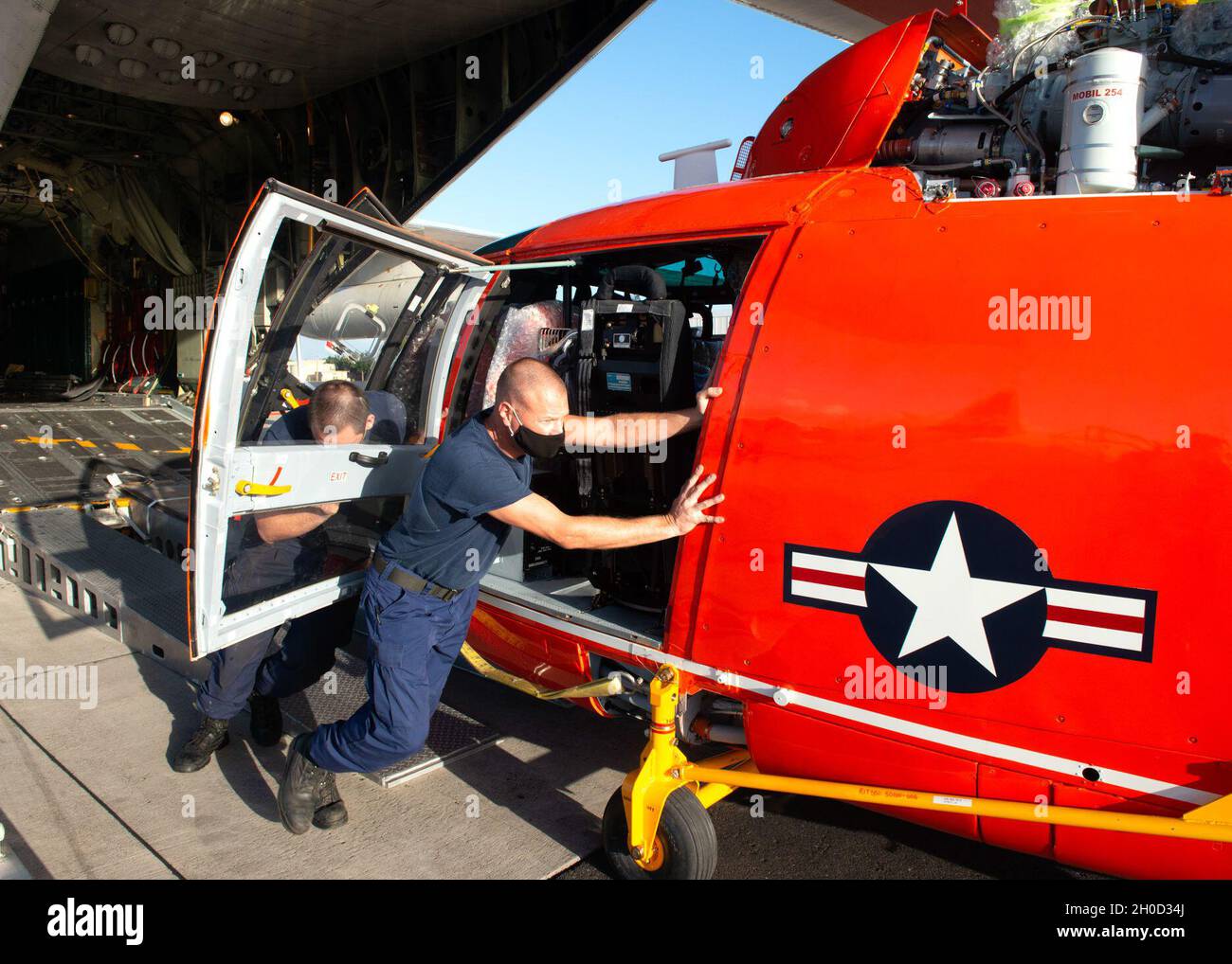 Un équipage de Barbers point de la station aérienne de la Garde côtière décharge un hélicoptère MH-65E Dolphin d'un avion HC-130 Hercules à Oahu (Hawaï), le 28 janvier 2021.Le modèle Dolphin 'echo' remplace l'ancien modèle 'delta'. Banque D'Images