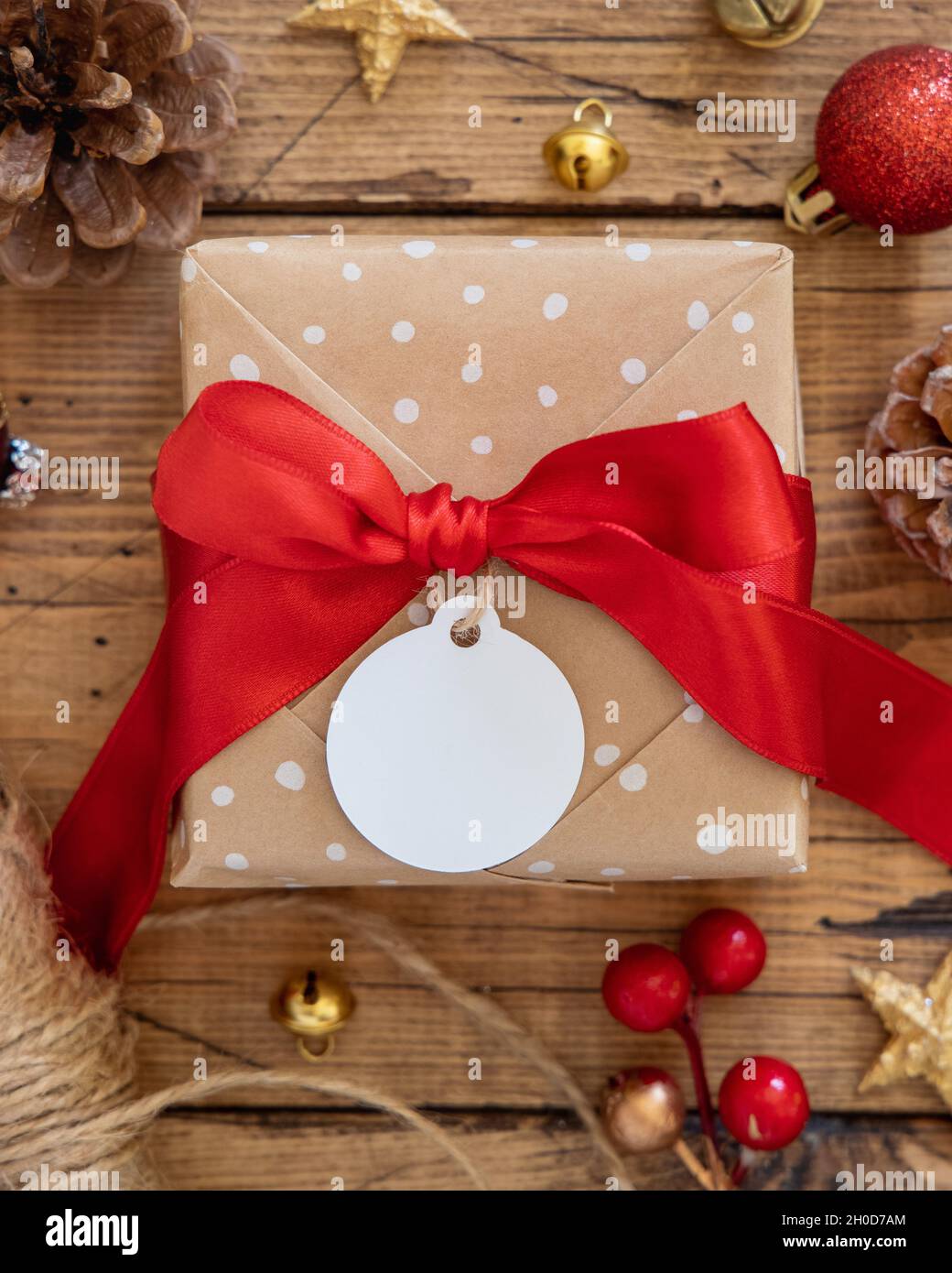 Boîte cadeau enveloppée de style rustique avec étiquette cadeau en papier  sur une table en bois marron et décorations de Noël rouges et dorées autour  de la vue du dessus.Nordic Winter compositi