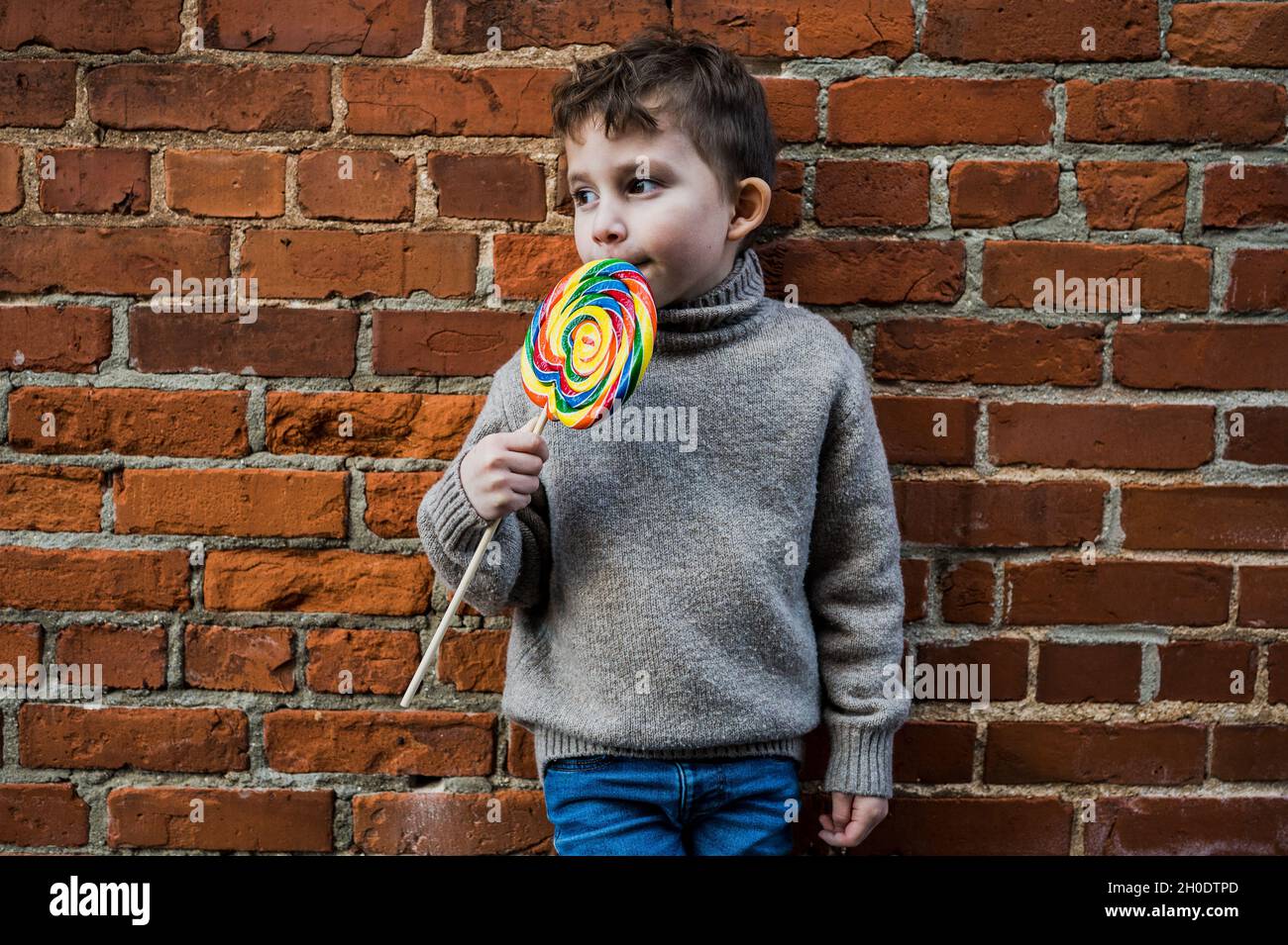 Petit garçon avec un Lollipop géant appuyé contre un mur de briques Banque D'Images
