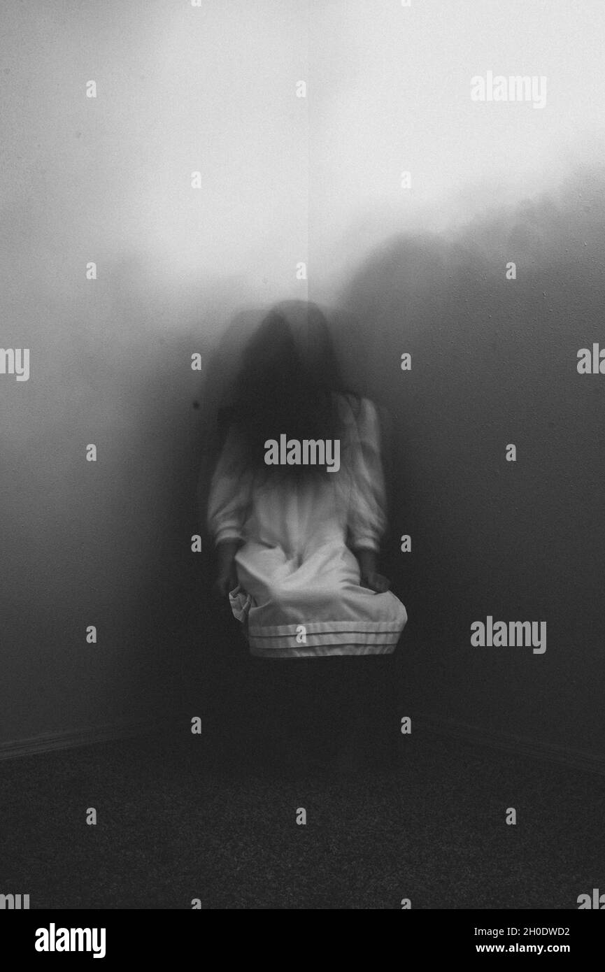 Une fille fantôme effrayante assise dans le coin de la chambre à la maison Banque D'Images