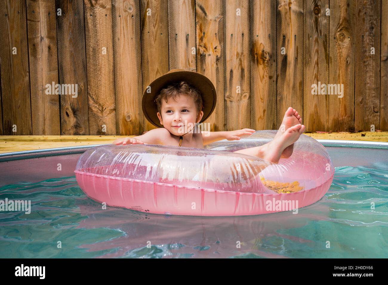 Un petit garçon dans un chapeau de cow-boy se rafraîchi dans une piscine arrière-cour. Banque D'Images