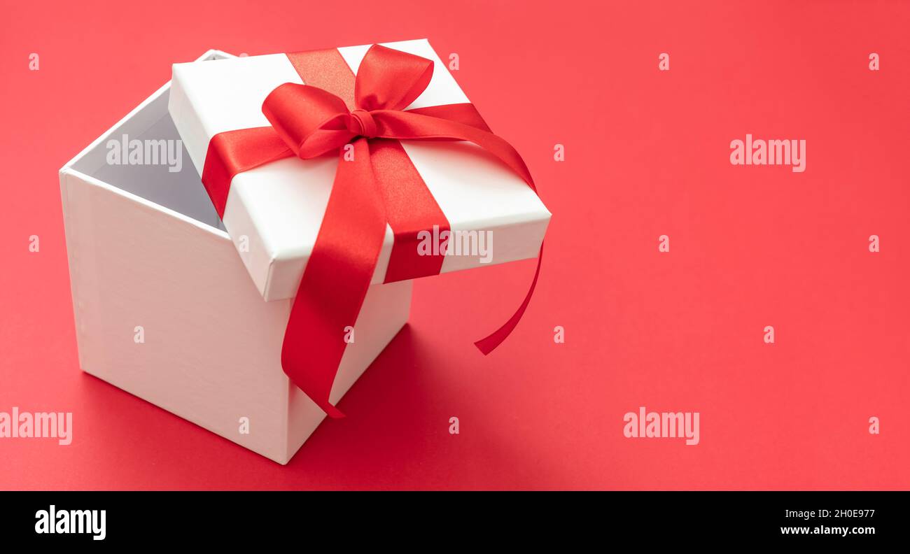 Boîte cadeau de Noël blanche avec ruban rouge noeud ouvert sur fond rouge, surprise de la Saint-Valentin, cadeau de vacances du nouvel an, décoration en satin curly.Copier Banque D'Images