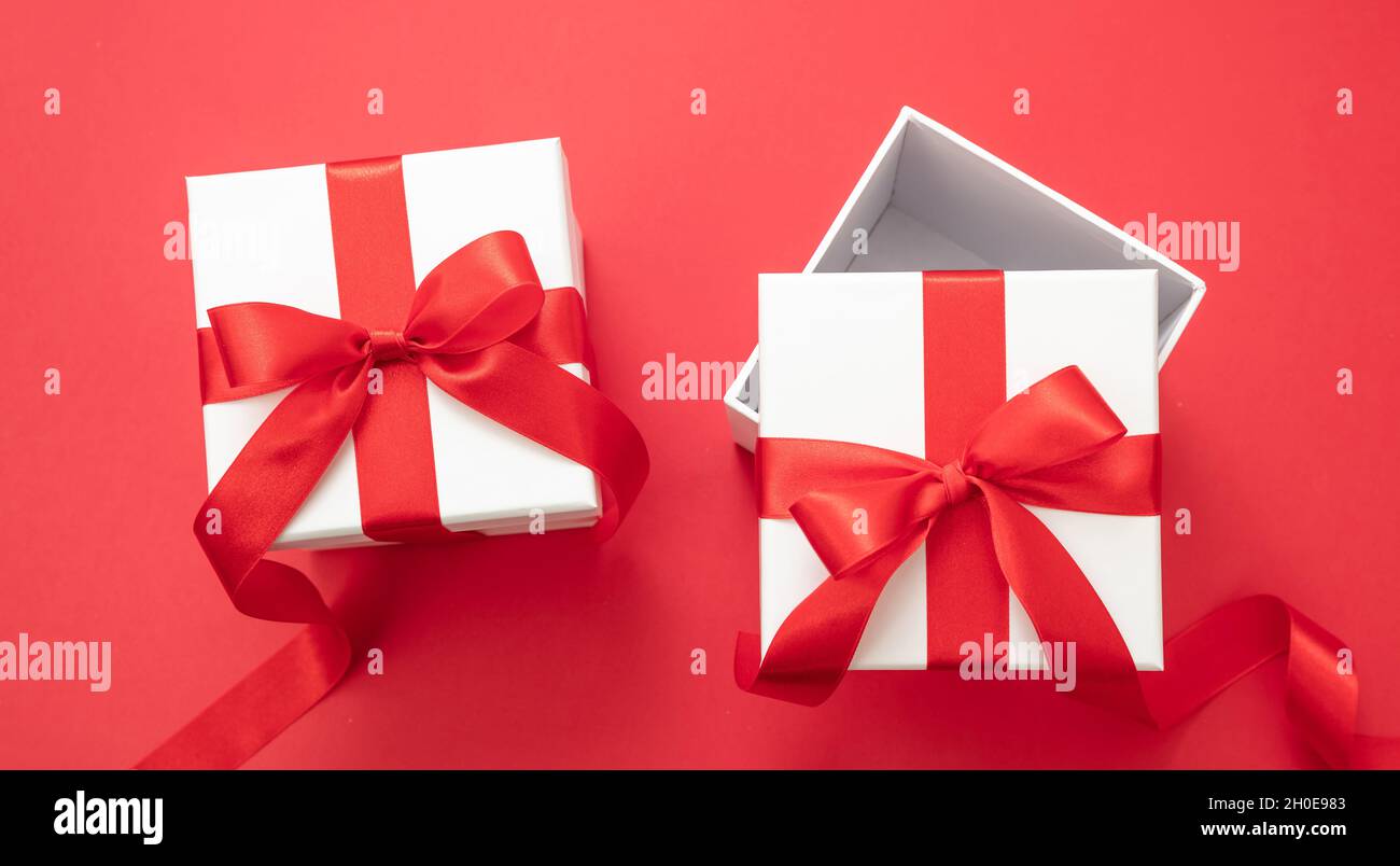 Noël présente surprise, deux boîtes cadeau de Saint-Valentin blanc avec ruban rouge noeud ouvert et fermé sur fond rouge couleur, nouvel an emballage pac Banque D'Images