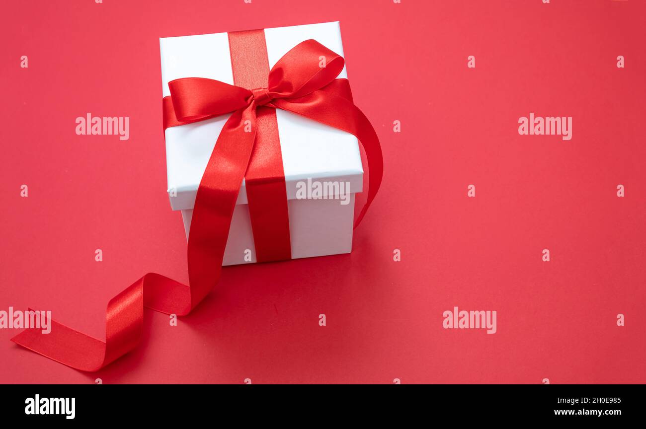 Boîte cadeau de Noël blanc noeud attaché avec ruban sur fond rouge, surprise de la Saint-Valentin, cadeau de vacances du nouvel an, décoration en satin.Copier la flèche Banque D'Images