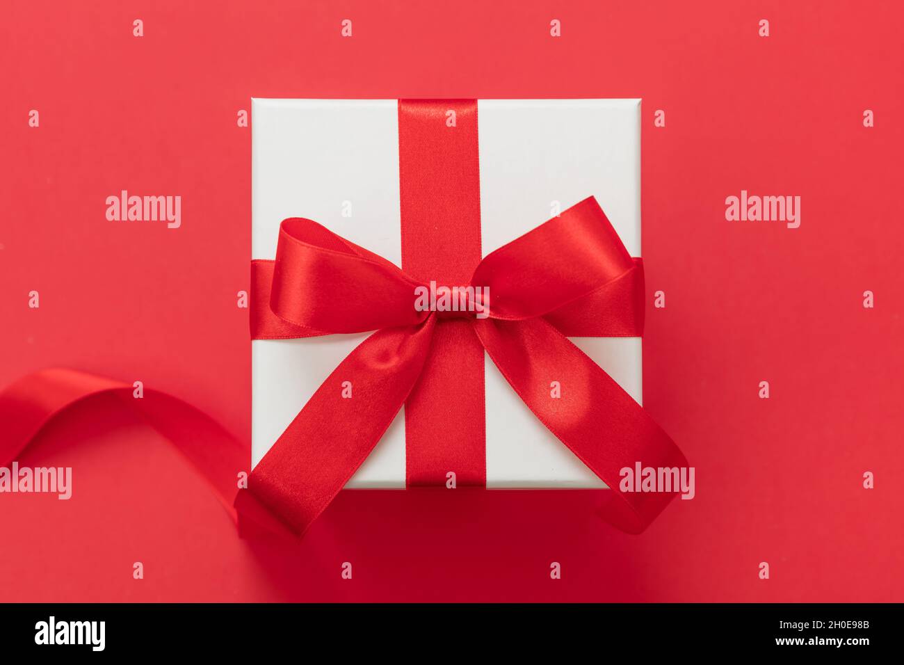 Boîte cadeau de Noël couleur blanche, noeud avec ruban rouge sur fond rouge, surprise de la Saint-Valentin, cadeau de Noël, décoration en satin Banque D'Images
