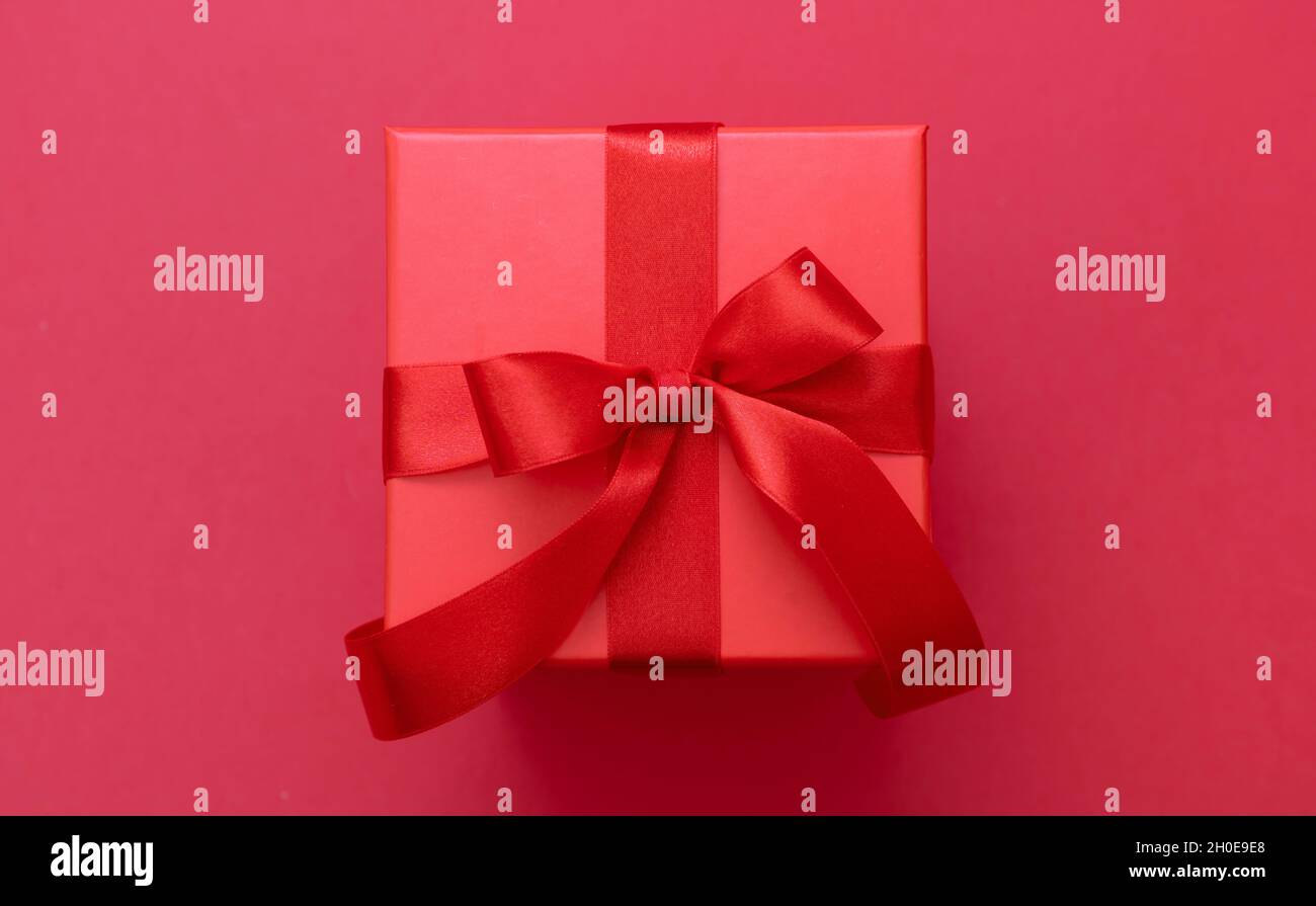 Boîte cadeau de Noël rouge noeud avec ruban sur fond rouge, surprise de la Saint-Valentin, cadeau du nouvel an, décoration en satin, vue du dessus. Banque D'Images