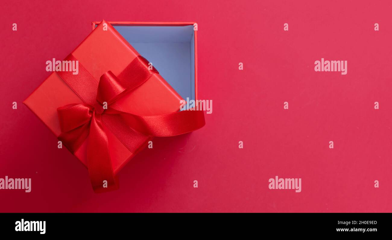 Boîte cadeau de Noël avec noeud en ruban ouvert sur fond rouge, surprise de la Saint-Valentin, cadeau de Noël, décoration en satin, vue du dessus.Copier Banque D'Images