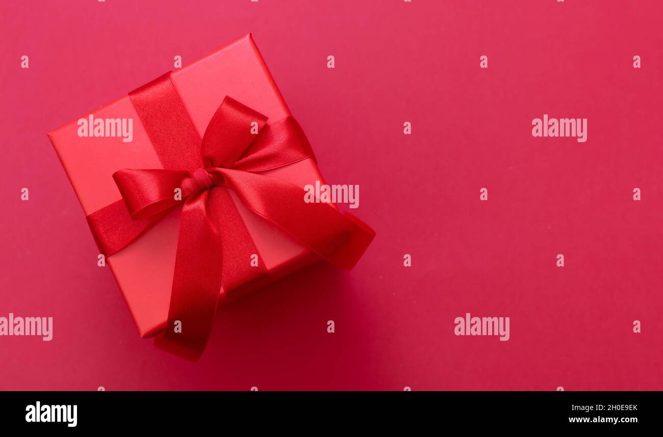 Boîte cadeau de Noël rouge noeud avec ruban sur fond rouge, surprise de la Saint-Valentin, cadeau du nouvel an, décoration en satin, vue du dessus.C Banque D'Images