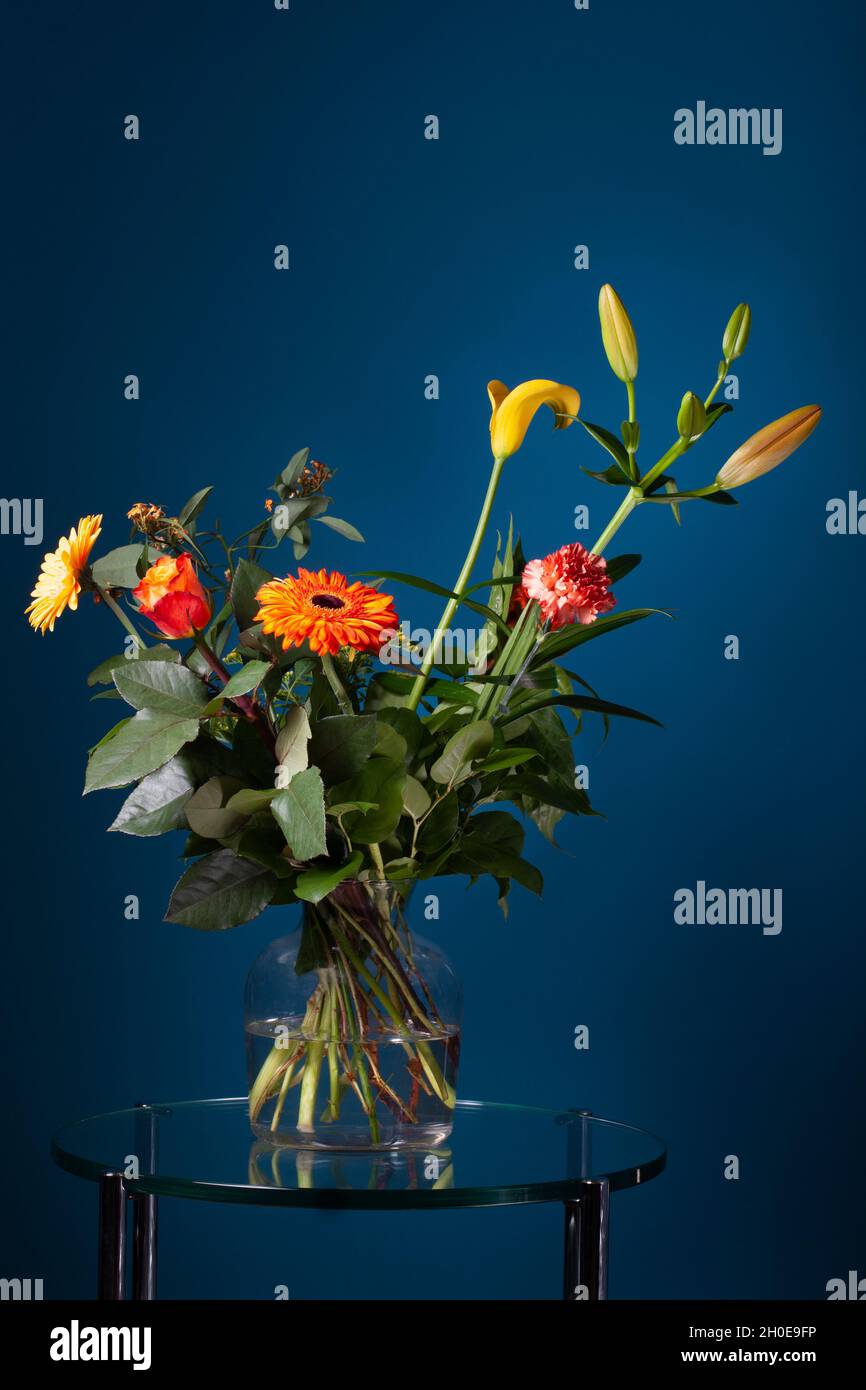 Bouquet frais de fleurs dans un vase en verre sur une table en verre avec un fond bleu foncé Banque D'Images