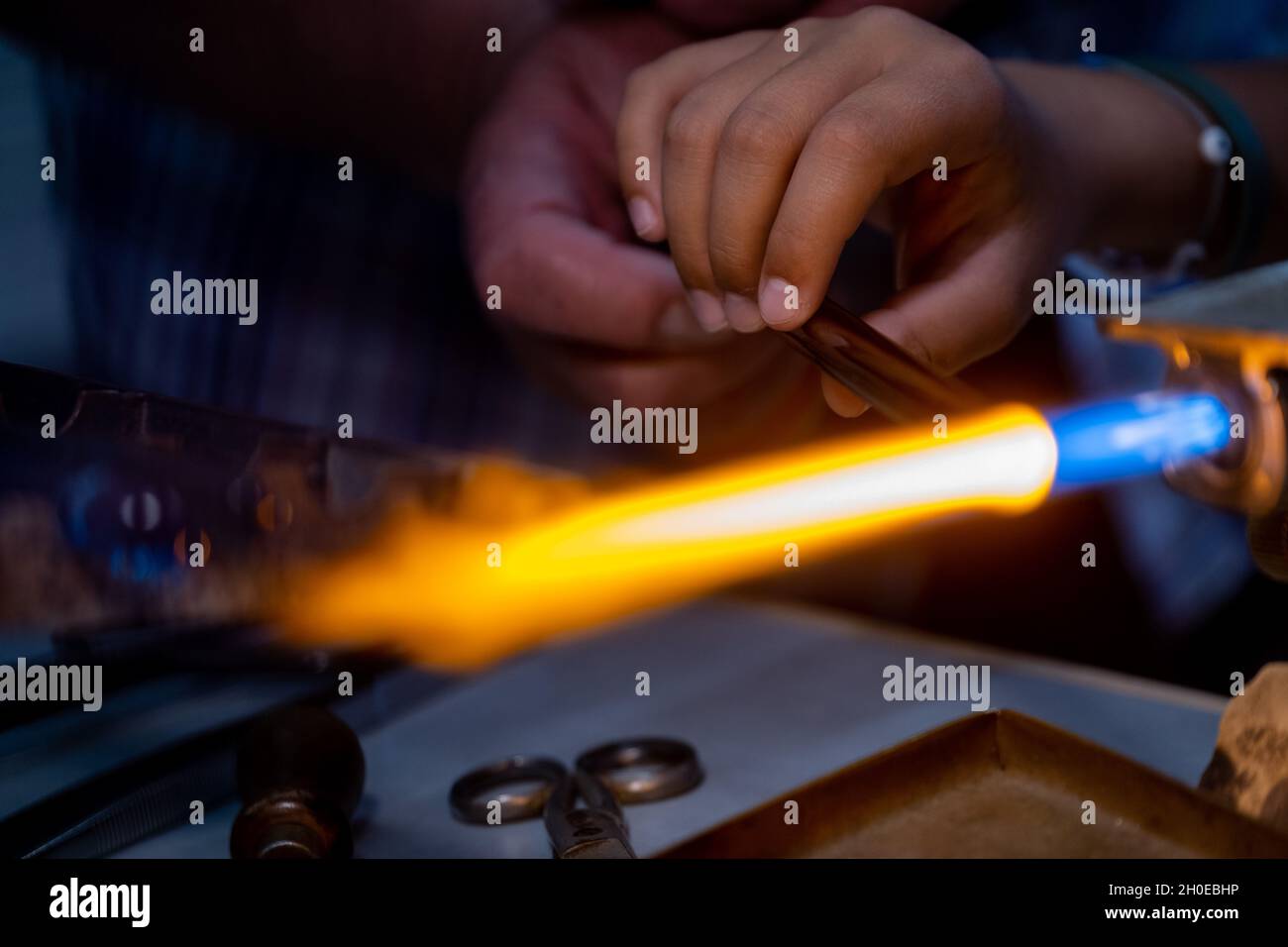 Main d'un travailleur de la flamme et main d'un enfant pendant la fabrication de perles de verre. Cet art a été inscrit en 2020 sur la liste représentative de l'intangible Banque D'Images