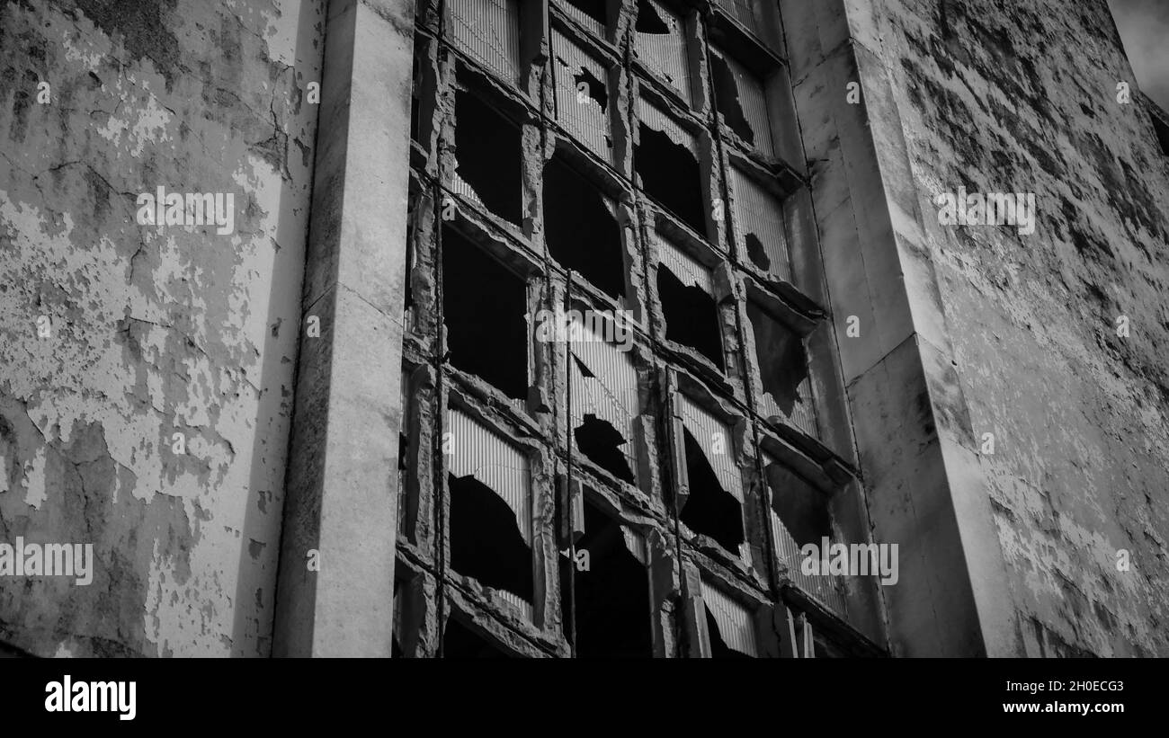 Photo en niveaux de gris d'anciennes fenêtres brisées d'un bâtiment abandonné - horr Banque D'Images
