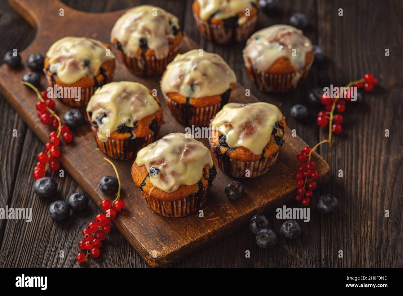 Muffins faits maison aux raisins de Corinthe rouges et aux bleuets, recouverts de garniture au chocolat blanc. Banque D'Images
