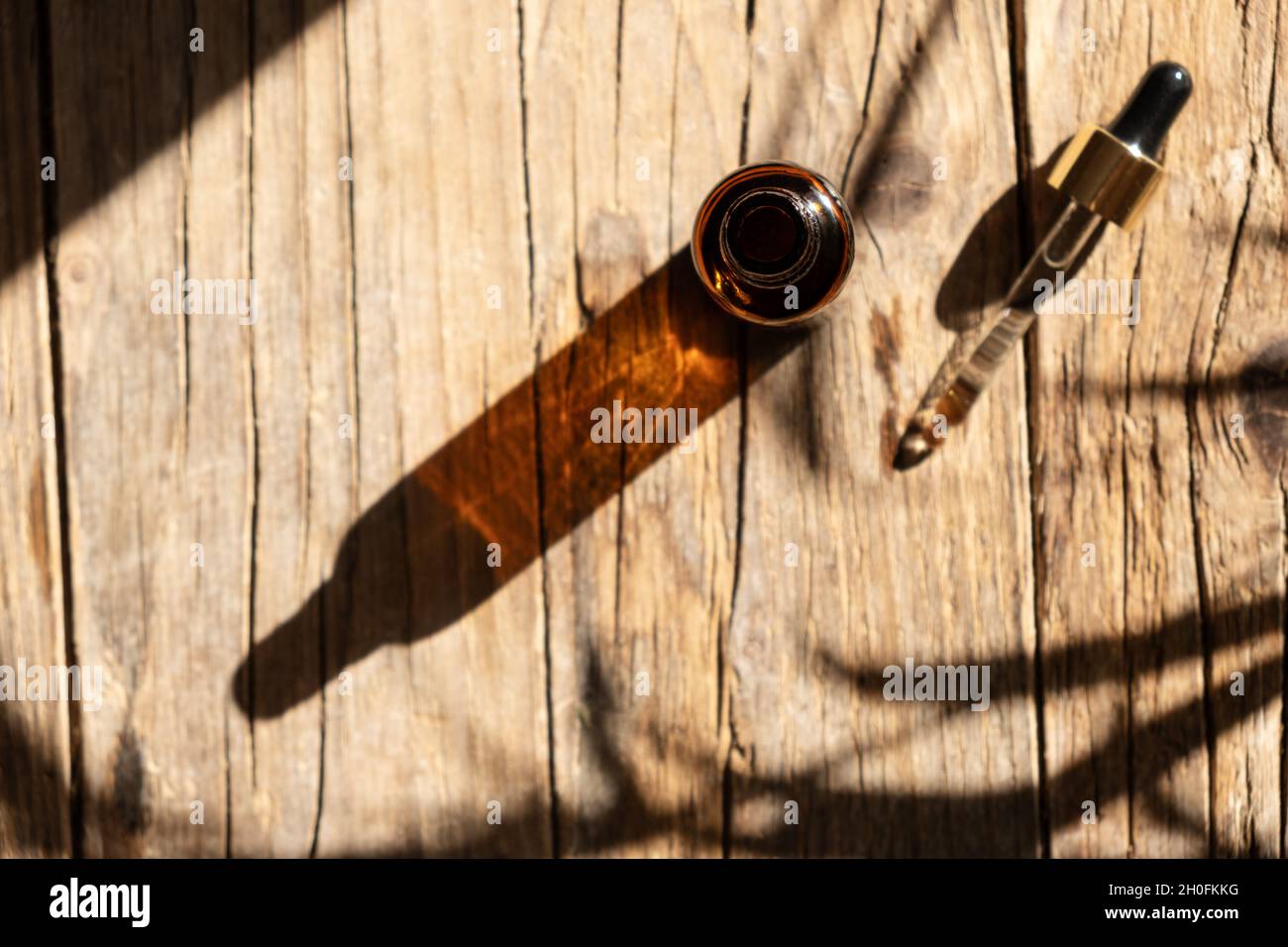 Flacon en verre ambré foncé avec compte-gouttes pour l'huile, la lotion ou le sérum sur un fond en bois vieilli avec une ombre dure de feuilles de palmier tropicales.Présentation d'un produit cosmétique.Aménagement du salon de beauté . Banque D'Images