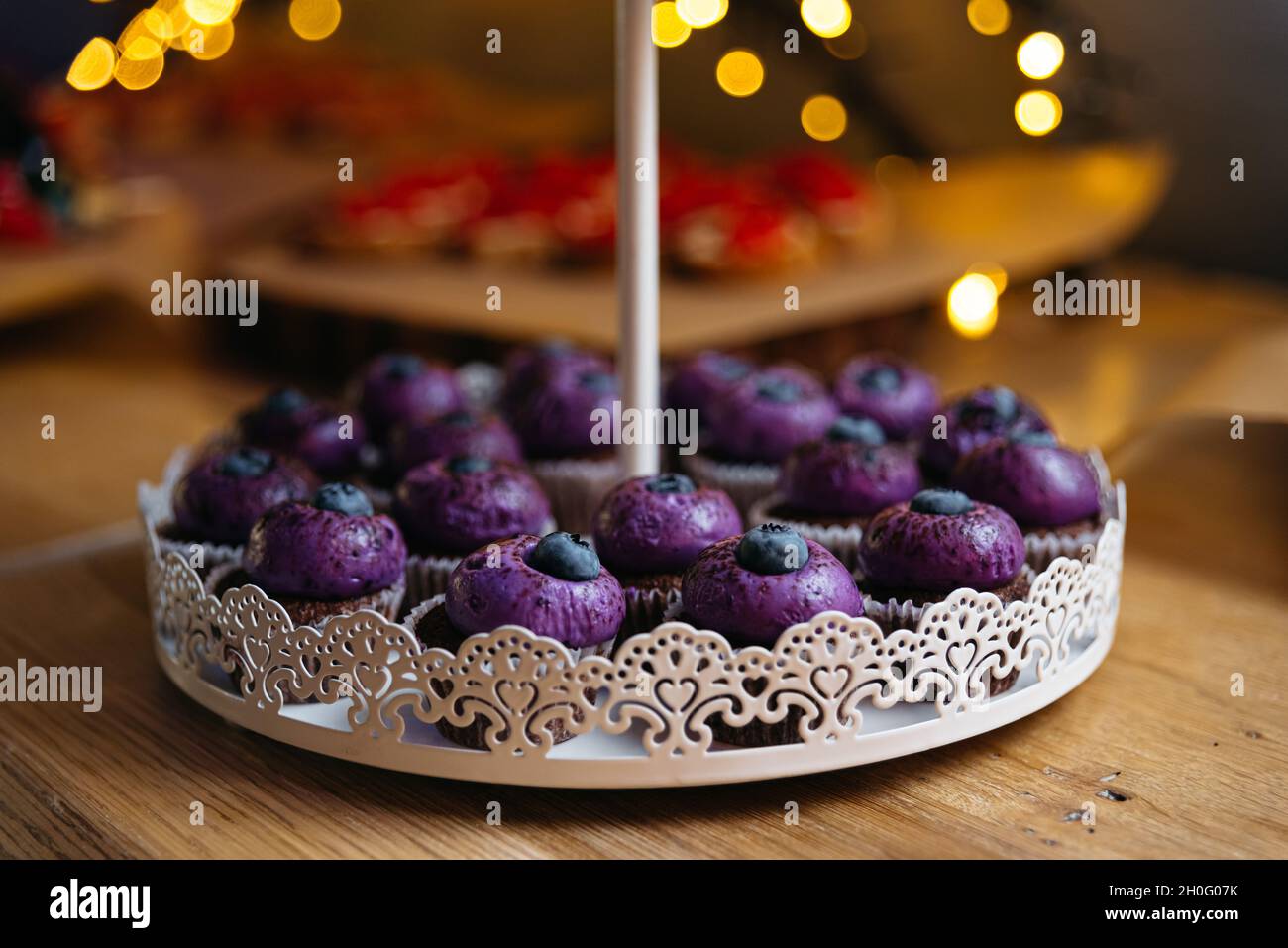 Cupcakes au chocolat avec crème pourpre et bleuets sur le dessus.En arrière-plan, effet bokeh des lumières jaunes. Banque D'Images