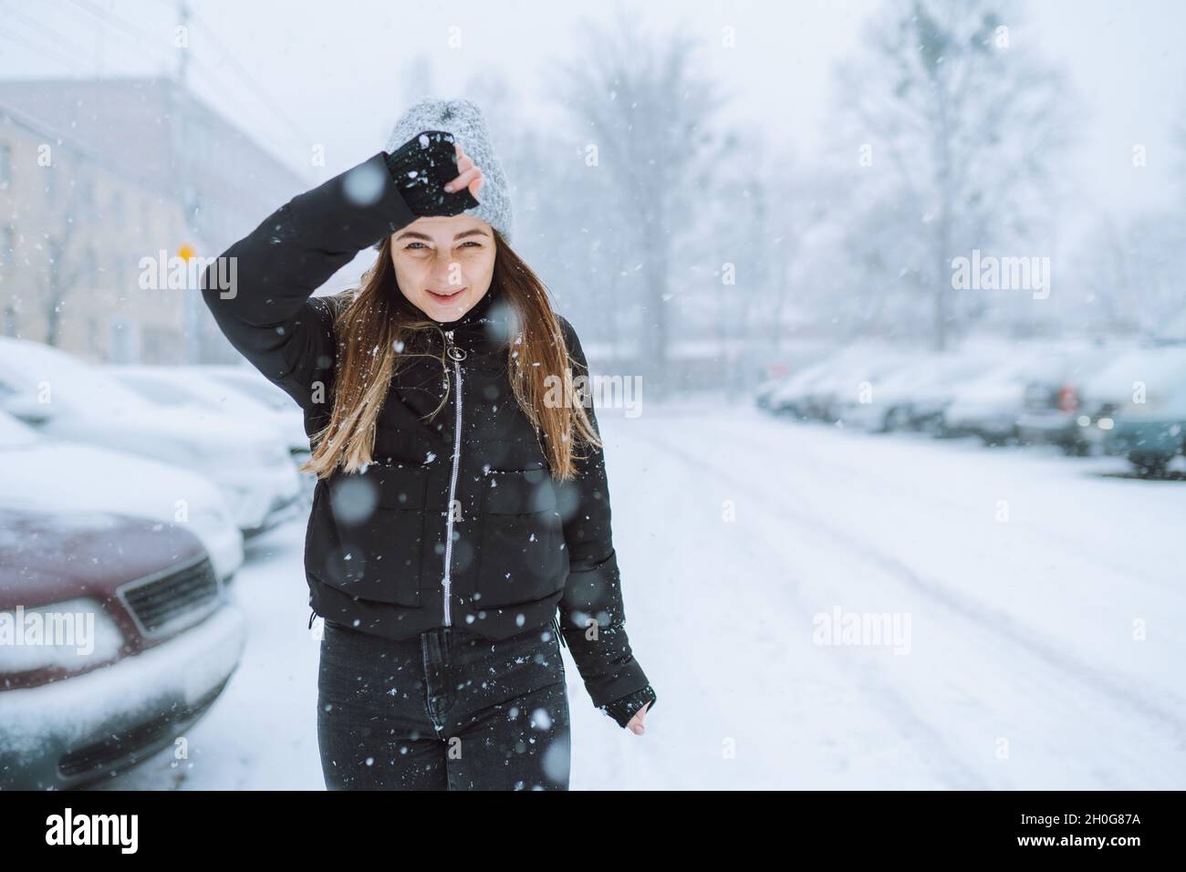 Portrait extérieur de la jeune femme dans la rue sous les chutes de neige.Mauvais temps froid, hiver venteux.Femme essayez de cacher son visage de la neige avec sa main. Banque D'Images