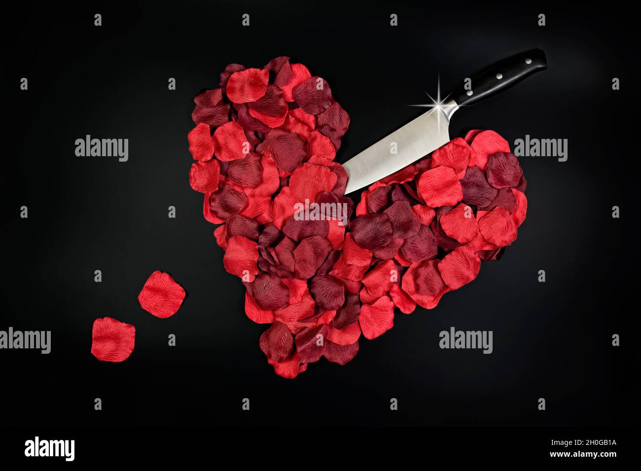 Pétales rouges en forme de coeur avec un couteau collé avec des pétales amples représentant des gouttes de sang, pris sur un fond blanc Uni Banque D'Images