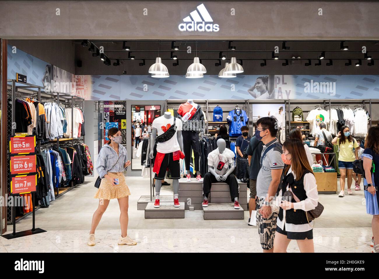 Les acheteurs marchent devant la marque allemande multinationale de vêtements de sport Adidas magasin et logo à Hong Kong. Banque D'Images