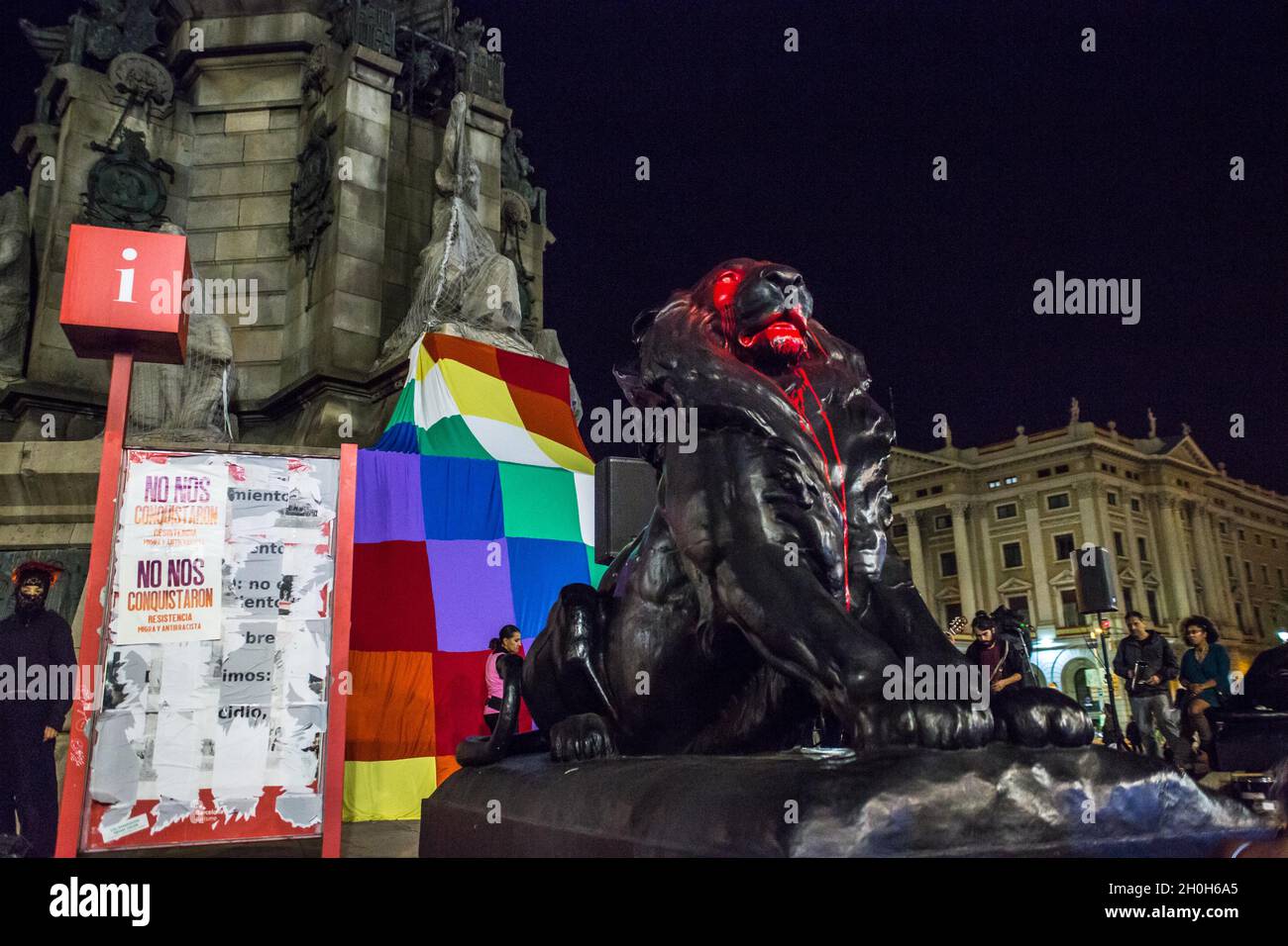 Barcelone, Espagne.12 octobre 2021.La statue du lion du monument de Christophe Colomb est visible sous la peinture rouge devant un drapeau de Wiphala.divers groupes anticolonialistes ont appelé une manifestation qui a quitté les Ramblas de Barcelone jusqu'à la statue de Christophe Colomb, avec les slogans « ils ne nous conquéront pas » et « rien à célébrer ».Les groupes ont protesté contre la célébration du 12 octobre, jour hispanique.Diverses présentations culturelles et représentations de peuples autochtones de pays d'Amérique latine et d'Afrique ont été réalisées.Crédit : SOPA Images Limited/Alamy Live News Banque D'Images