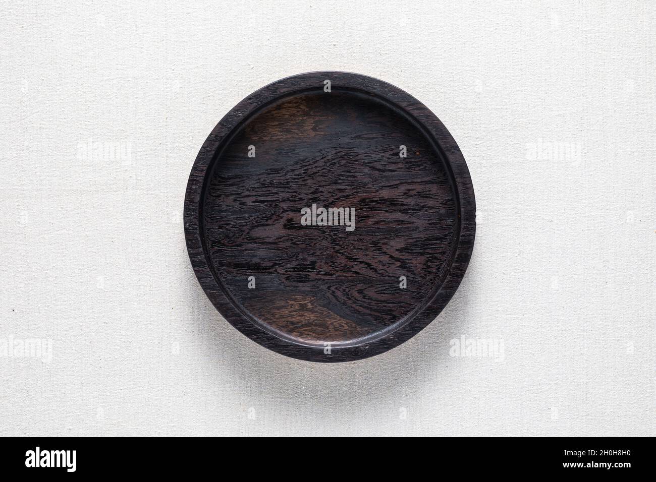 Assiette ronde en bois noir foncé à la main sur toile de jute.Plateau rond Banque D'Images