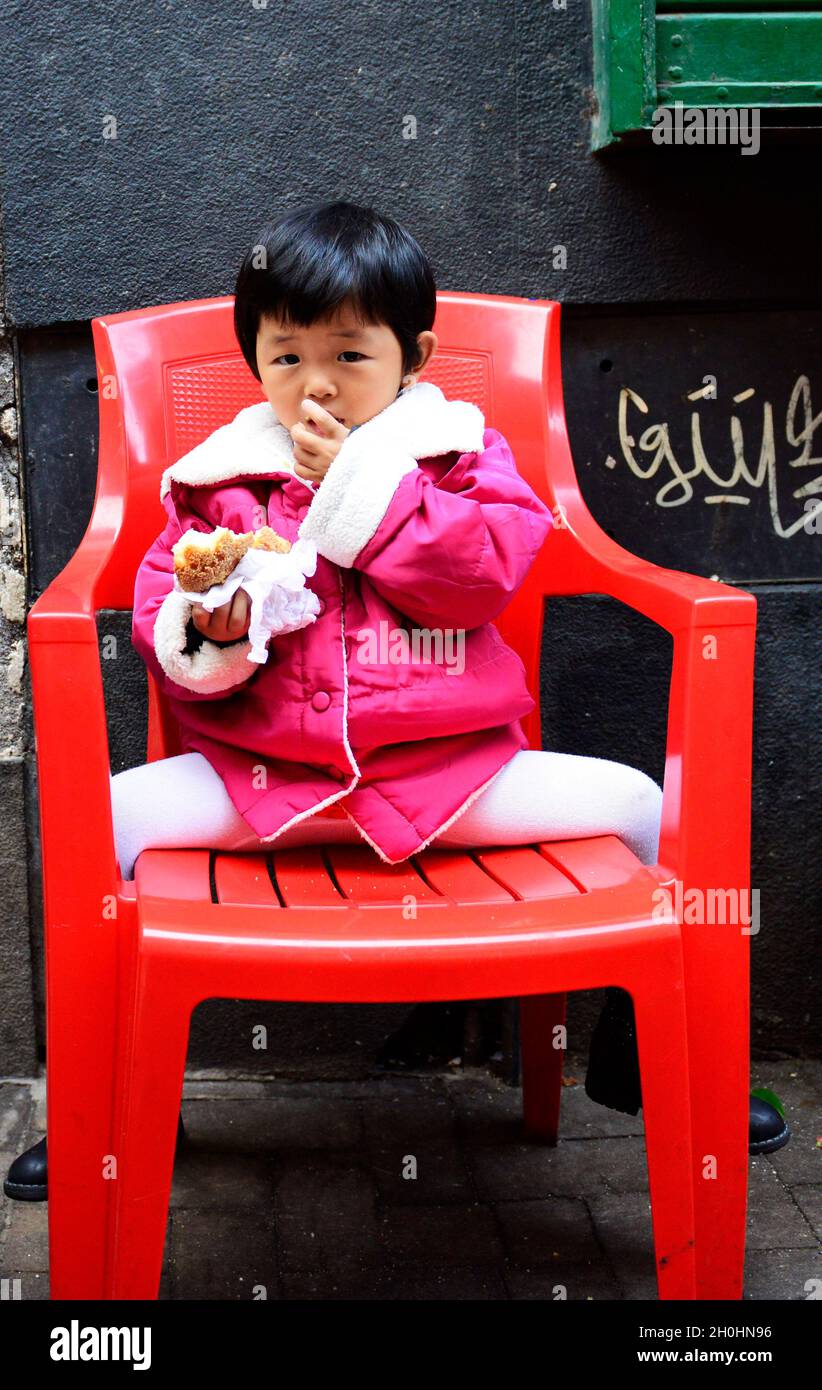 Une mignonne fille chinoise assise sur une chaise au marché de Catane, en Italie. Banque D'Images