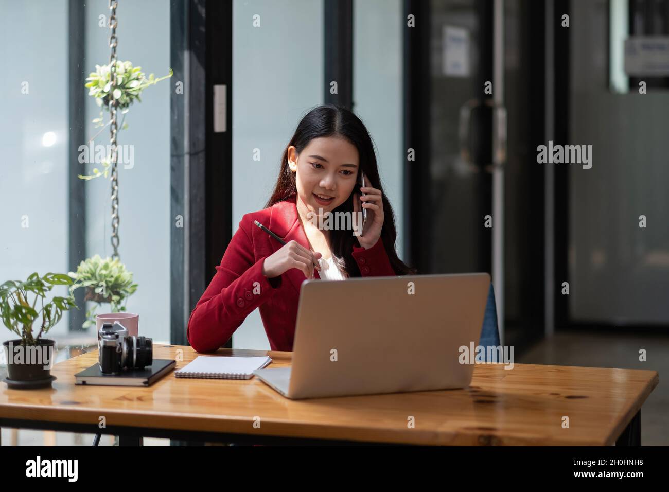 Femme d'affaires souriante au travail parlant au téléphone, femme asiatique assise et travaillant financier avec un ordinateur portable Banque D'Images