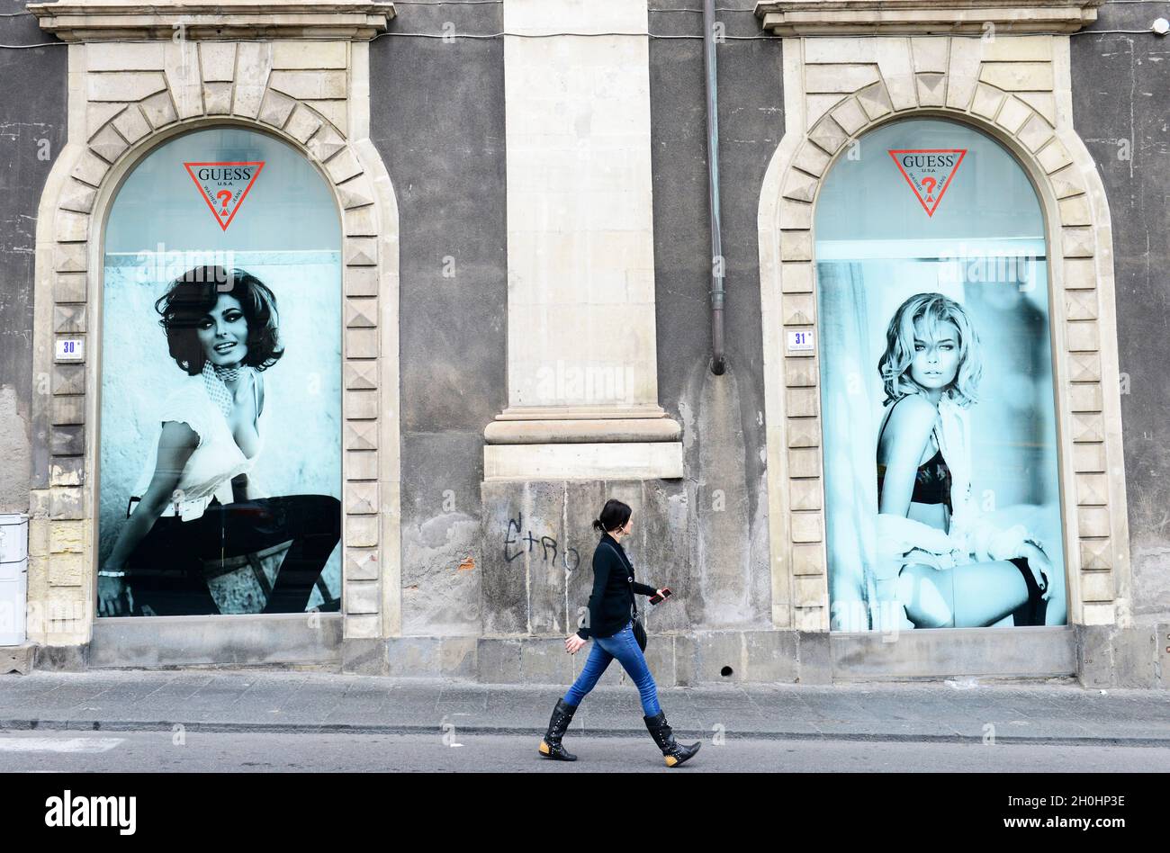 Une italienne marchant sous une grande publicité de la boutique de vêtements Guess au Palazzo Tezzano à Catane, Italie. Banque D'Images