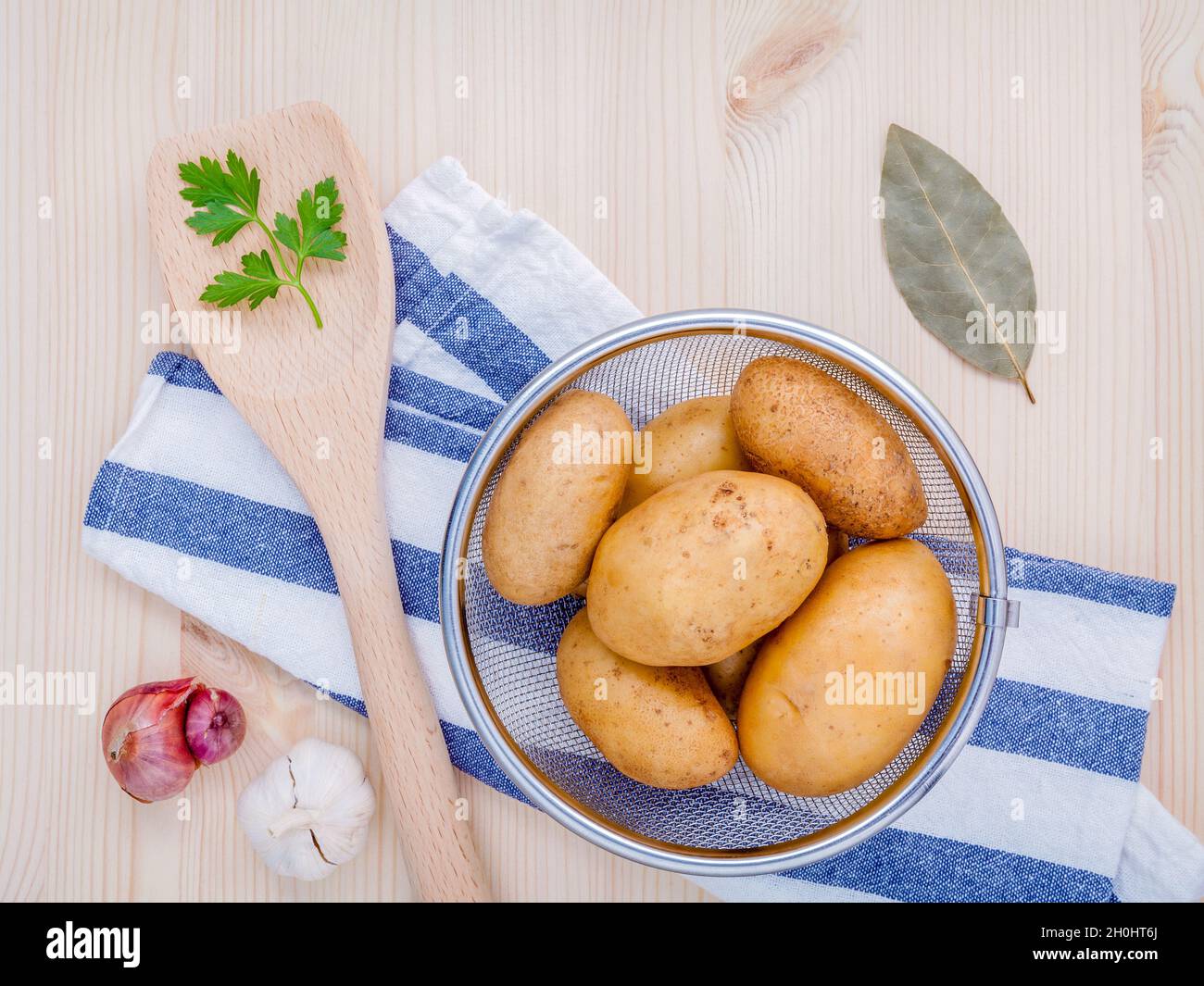 Des pommes de terre biologiques frais dans panier avec herbes ail échalote,,le persil et les feuilles de laurier sur table en bois rustique. Préparation à la cuisson. Banque D'Images