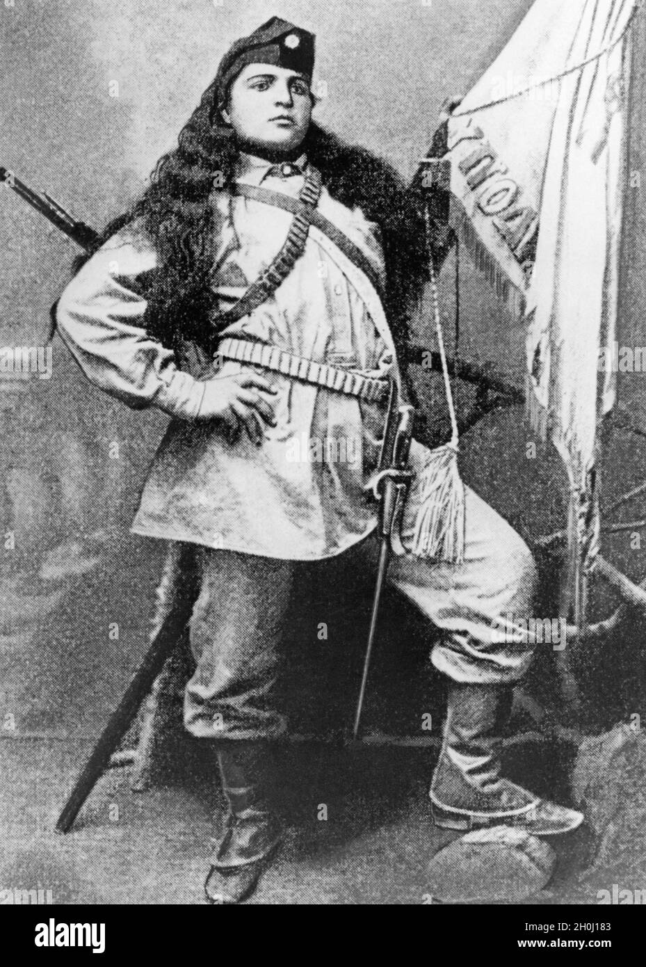 Un combattant volontaire dans la guerre turco-grecque pose armé à côté du drapeau grec.[traduction automatique] Banque D'Images