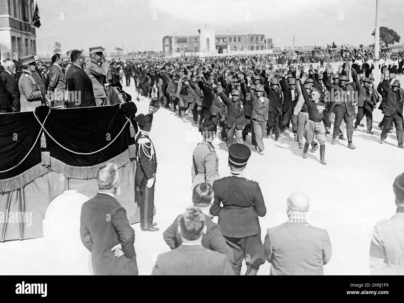 Lors d'une visite du roi d'Italie, Victor Emmanuel III, à Littoria (aujourd'hui Latina) en 1933, les ouvriers agricoles et les ouvriers du bâtiment ont organisé un défilé devant lui.Tous salués avec le saluto romano.Les travailleurs ont érigé de nombreux bâtiments dans la ville planifiée récemment fondée de Latina au cours de ces années.En arrière-plan, on peut voir l'école élémentaire de la ville, récemment construite sur la Piazza Dante.[traduction automatique] Banque D'Images