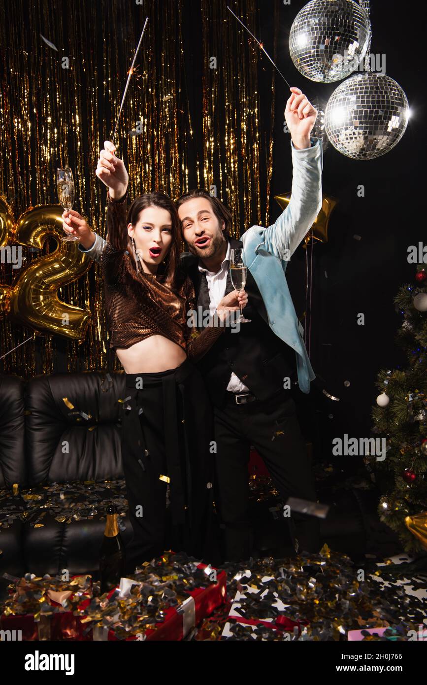 un couple enchanté avec des sparkers et des verres à champagne célébrant noël en noir Banque D'Images