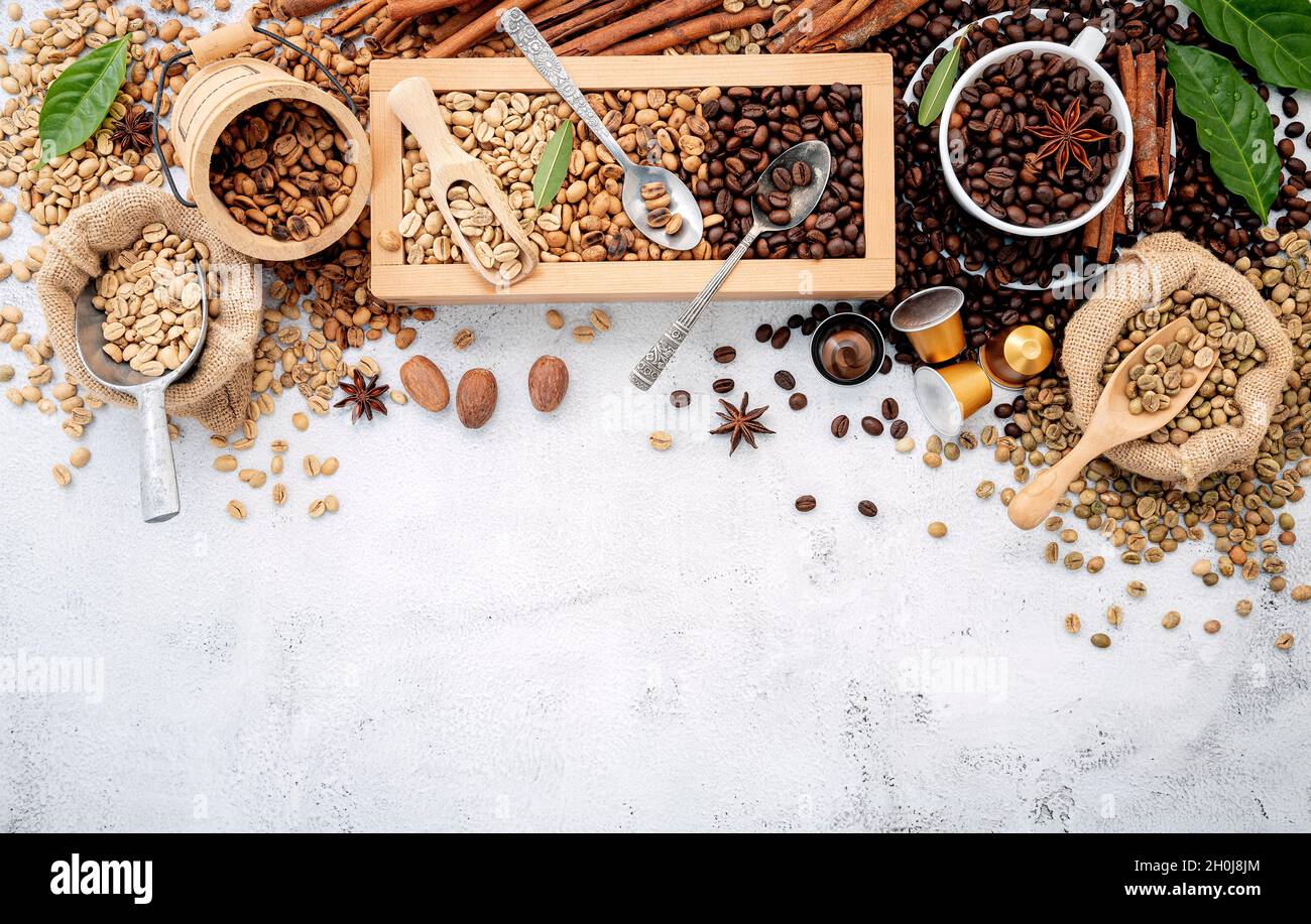 Grains de café décaféiné vert et brun non torréfiés et torréfiés foncé dans une boîte en bois avec des pelles sur fond de béton blanc. Banque D'Images