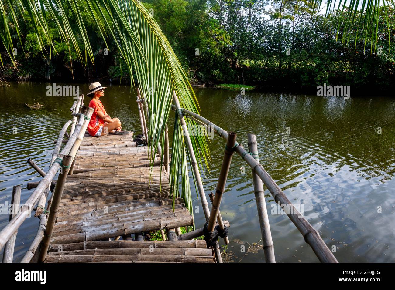 La femme est assise à la fin d'un quai de bambou regardant Banque D'Images
