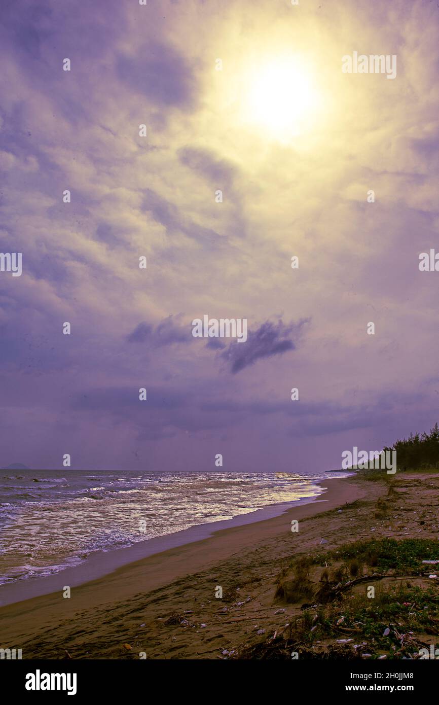 Un jour de mauvaise humeur sur une plage vietnamienne avec des nuages bleu foncé de lavande et un soleil jaune. Banque D'Images